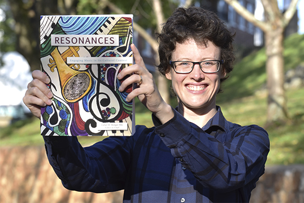 Esther Morgan-Ellis holding a copy of her open-access textbook, Resonances